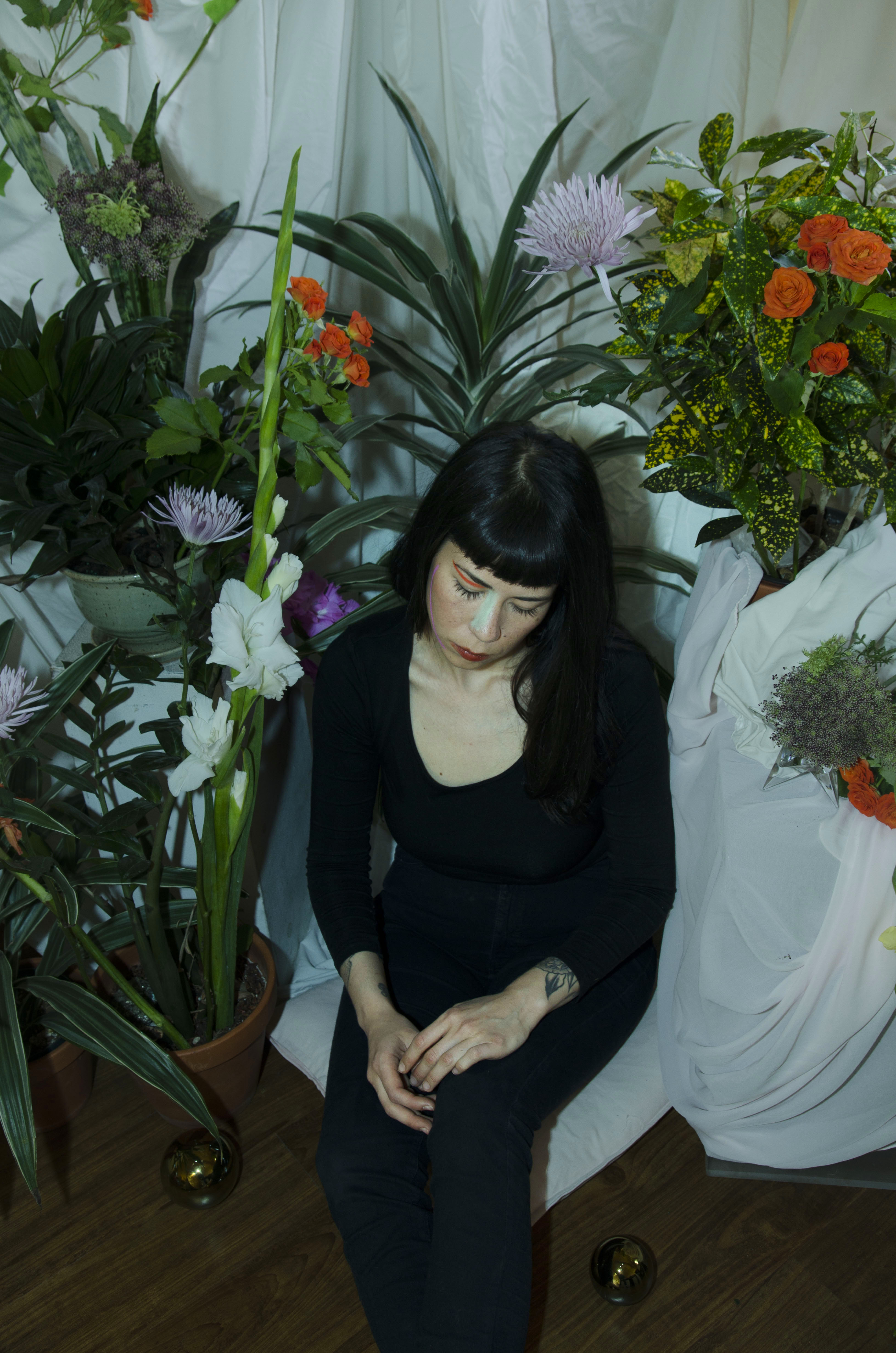 A photo of Chloe Alexandra Thompson sat in a room surrounded by plants and flowers