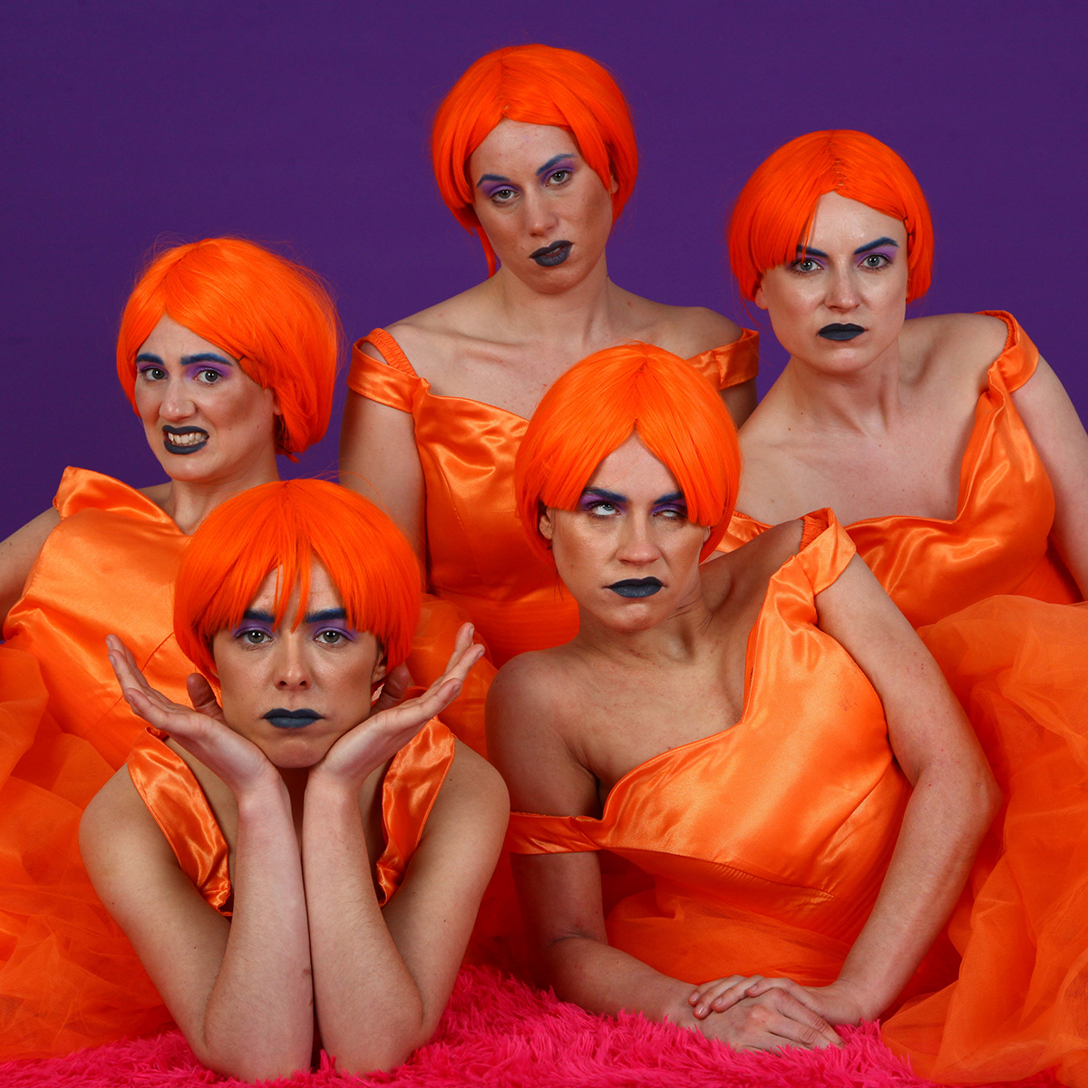 A photo of Figs in Wigs performers. Five people in orange, bob blunt cut wigs and orange dresses, each pulling a different, funny expression.