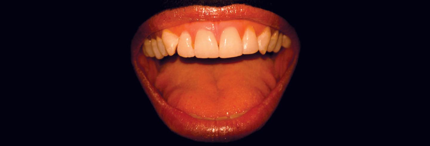 A photo of teeth, tongue and open mouth on a black background.
