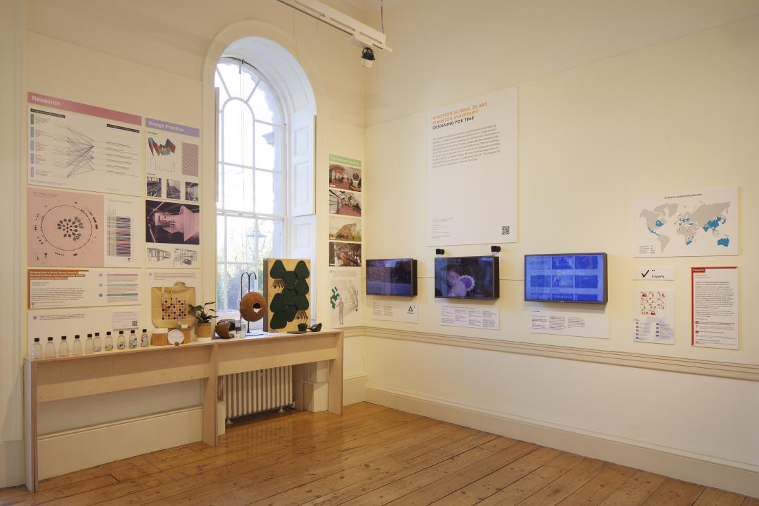 An installation view of Kingston University's display. There are diagrams pinned to the wall alongside a cabinet with miniature models of prototype looking things.