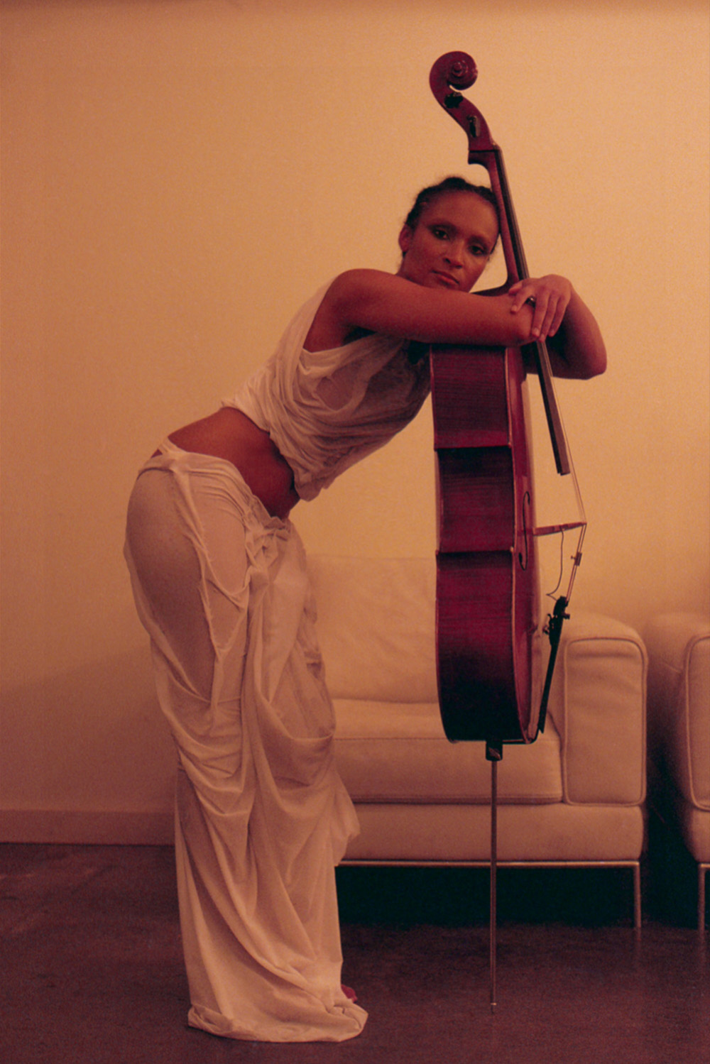 A photo of Ouri, wearing a white long skirt and top, posing with a cello
