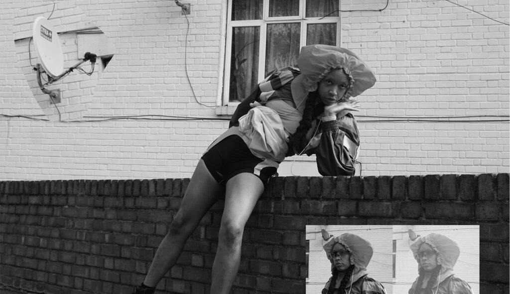 A black and white photo of GLOR1A. She is leaning on a brick wall and posing to camera.