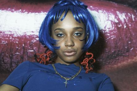 A photo by Eileen Perrier shows a confident young woman with blue bobbed hair lookign directly at the viewer 