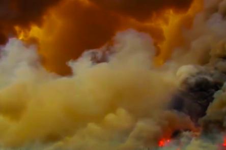 A still from Alberta Whittle's 'from the forest to the concrete'. The image is a wide angle shot of smoke billowing in huge cloud formations. In the bottom right the fire creating the smoke can be seen burning intensely.