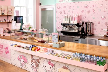 The Cute Coffee Shop by ARTBOX at Somerset House. A counter stacked with cute cakes, drinks and snacks is positioned in a pink and pastel green room with Hello Kitty and friends decorating the walls.
