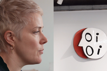A film still from Emma Hart: Language and Class. On the left hand side is a profile view of the artist Emma Hart, a woman with short blonde hair, who is mid-speech. On the right-handside is a ceramic artwork that spells OI OI