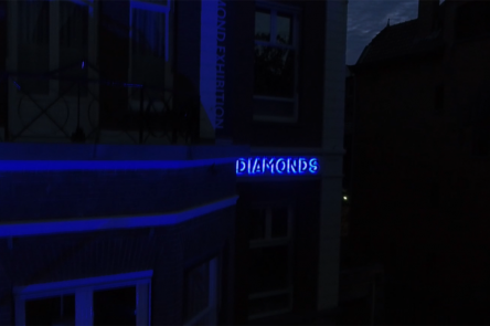 A still from Gerda Paliušytė's film. It depicts a blue neon sign on a building that says 'diamonds'