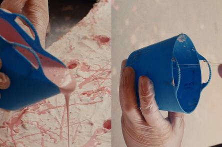 A still from the film Holly Hendry: The Art of Chaos. Gloved hands are shown pouring a pastel pink thick substance from a blue container into a textured white surface.