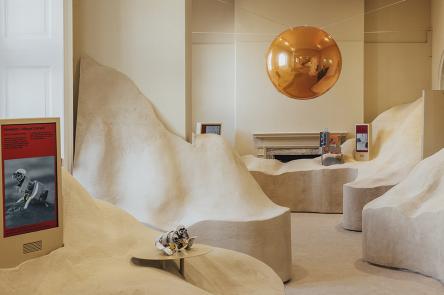 An installation view of Dubai's pavilion at London Design Biennale 2023. Towers of sand are piled high in a room, with a pathway cutting through the middle. 
