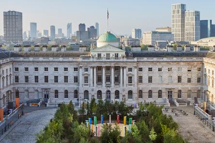 Forest for Change at Somerset House. Green leafy trees fill the courtyard. In the background you can see the London skyline and blue skies.