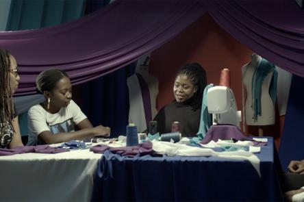 Artist Mary Sibande sitting in a textile studio talking to three women about her work