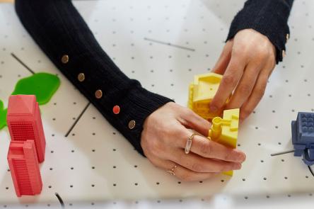 A visitor to the Now Play This projects her hands through a screen to adjust two yellow blocks on a board cut with pin holes. Photo by Ben Peter Catchpole