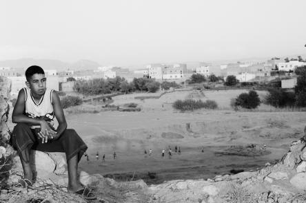 A black and white photo of a boy sitting on the broken remains of a wall that has been damaged and knocked down.