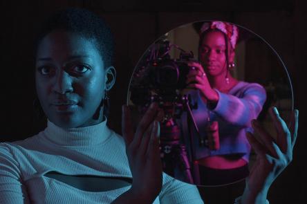 A still from the Future Producers' film Rising: A Manifesto. A Future Producer, Kayleigh, holds a circular mirror up to the camera. In the reflection you can see another Future Producer, Jahnavi, operating the camera capturing the image. 