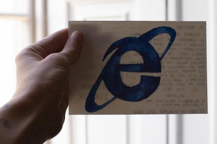 A photo of a hand holding a postcard. On the front of the postcard is the letter e in blue.