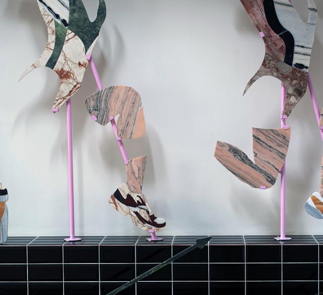 Sculpture of running legs and trainers on a black tiled platform in an art gallery