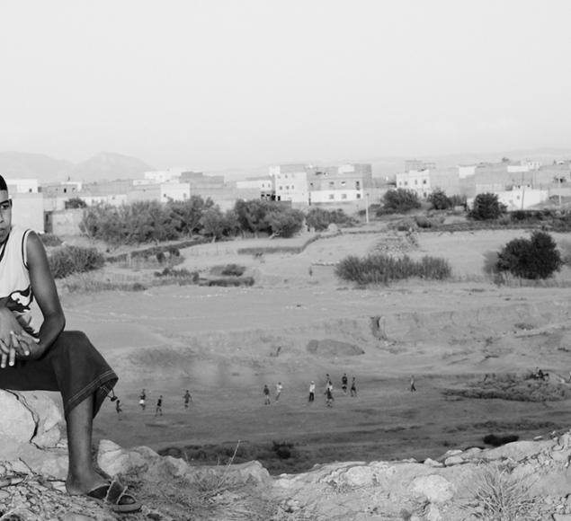 A black and white photo of a boy sitting on the broken remains of a wall that has been damaged and knocked down.