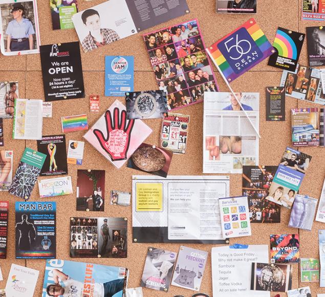 Installation view of UK Gay Bar Directory. The image shows an artwork presenting flyers and flags from different gay bars.