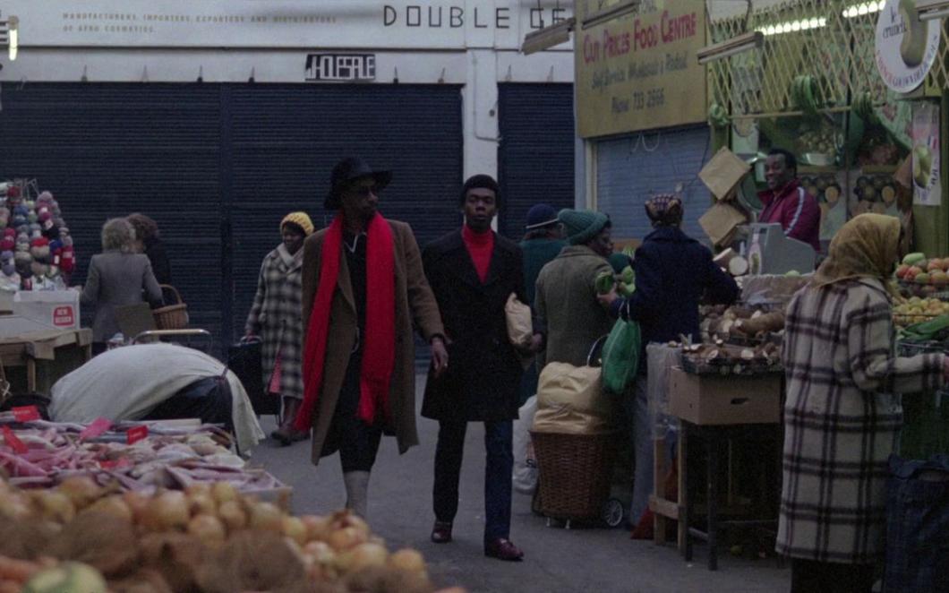 A still from the film Babylon showing two Black men walking through a covered market in South London