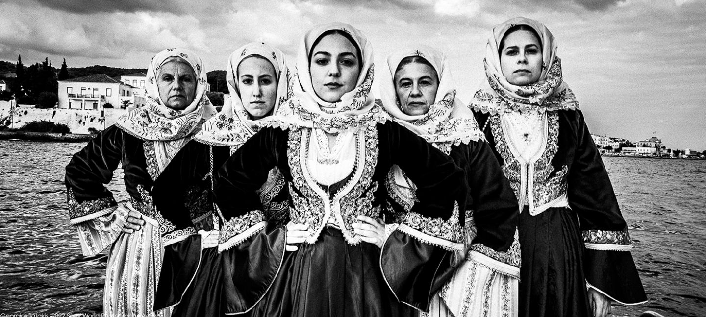 A photo by Georgios Tatakis, one of the selections for the Sony World Photography Awards exhibition 2022. It is a black and white photo of five women wearing traditional Greek dress. Each woman stares intensely at the camera.
