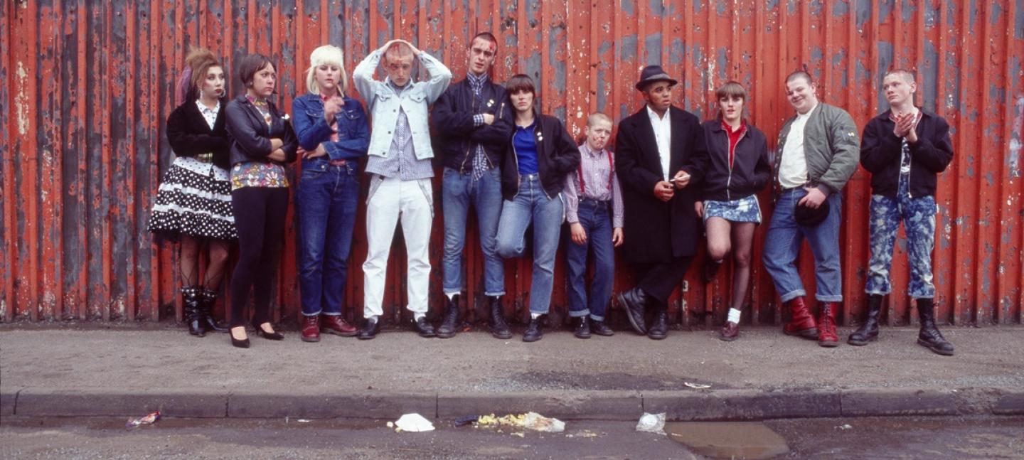 Film still of a group of people standing against a wall