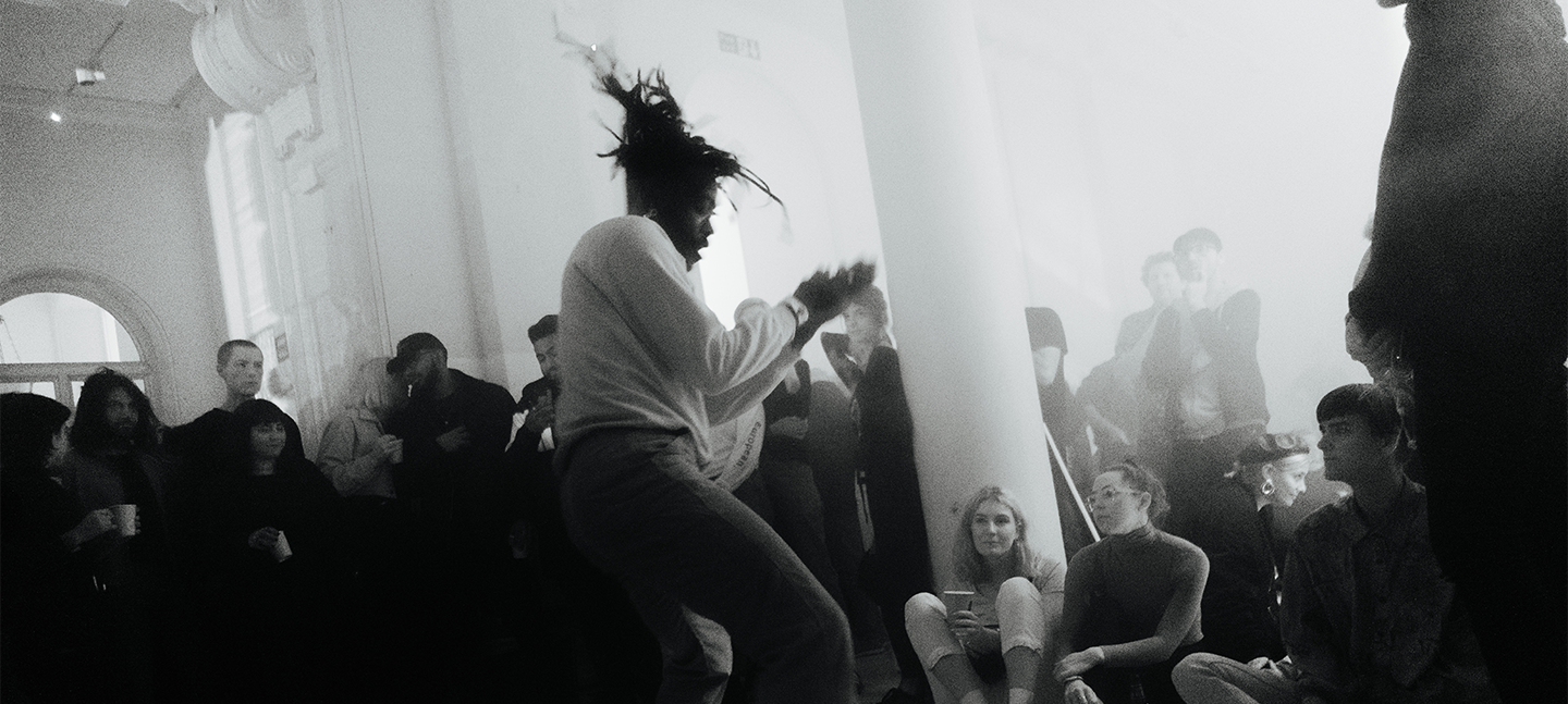 A black and white photo of Rowdy SS performing at AGM a few years ago. He is dancing, as a crowd of people watch on, enjoying themselves.