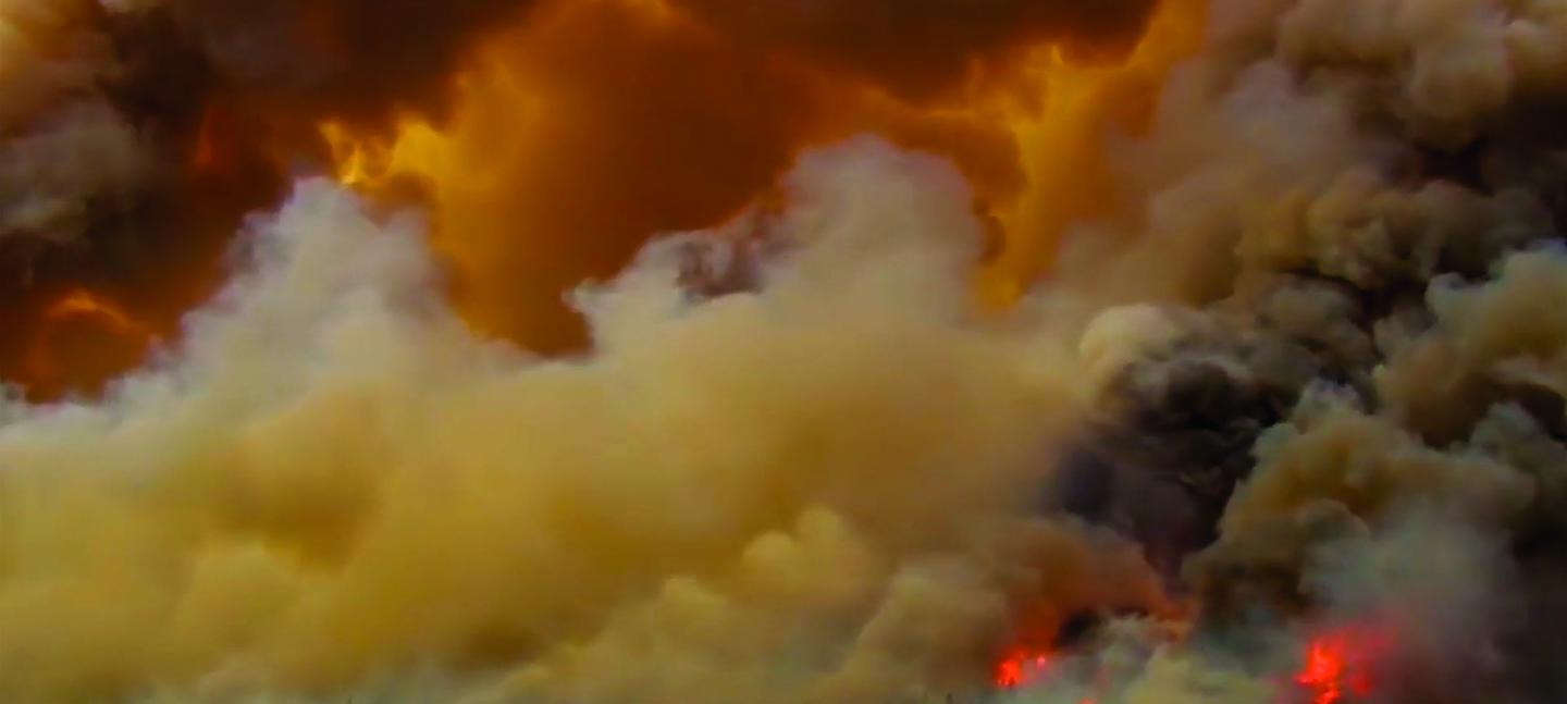 A still from Alberta Whittle's 'from the forest to the concrete'. The image is a wide angle shot of smoke billowing in huge cloud formations. In the bottom right the fire creating the smoke can be seen burning intensely.