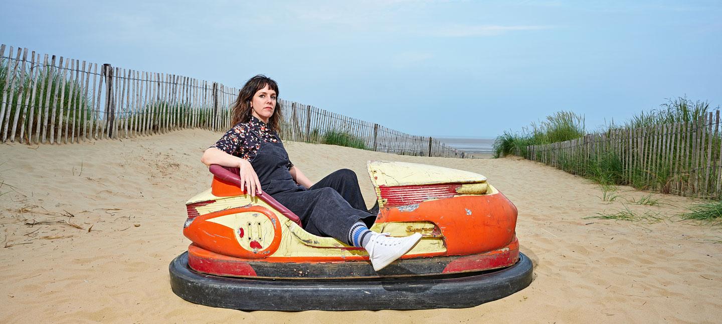 Anna Meredith, Bumps Per Minute album cover shows Anna sitting in a dodgem amongst some sand dunes © Mike Massaro