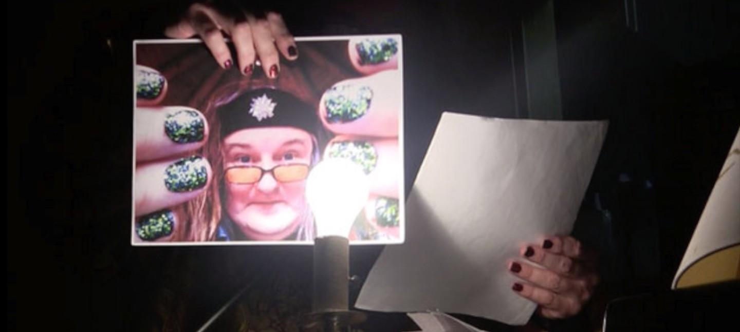 Someone holding up a photo of a woman in a headband and glasses to the camera, with a lit light bulb in front.