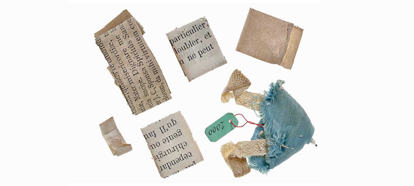 A photo of scraps of paper, folded neatly with typed French letters on them, alongside a scrap of turquoise fabric.