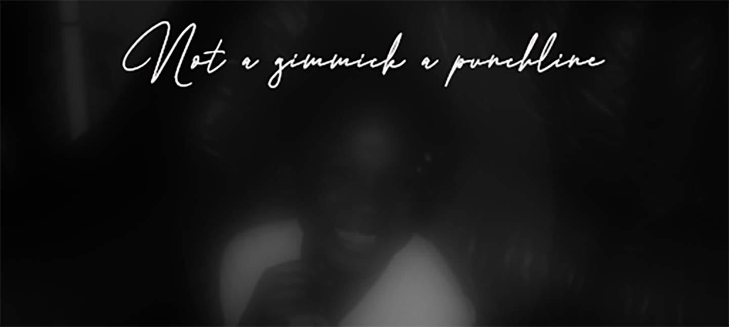 A black and white image of a blurred face wearing a white t-shirt and smiling. Above the image are the words 'Not a gimmick a punchline' in cursive writing