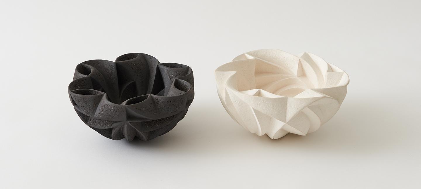 Artwork by Halima Cassell. Two ceramic, bowl-like structures with intricate moulds. On in black, the other in white..