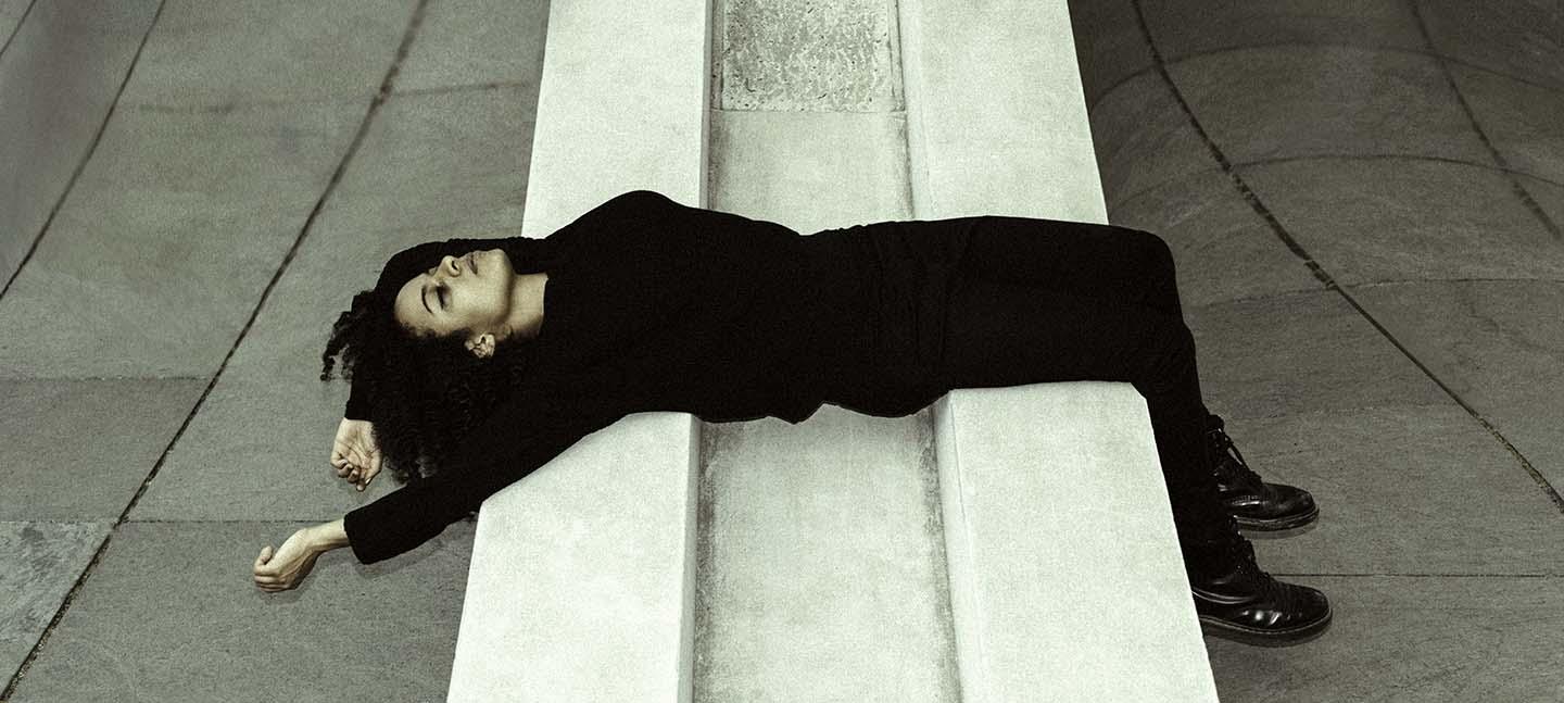Jessica Ekomane in a black suit laying on her back on a white stone structure