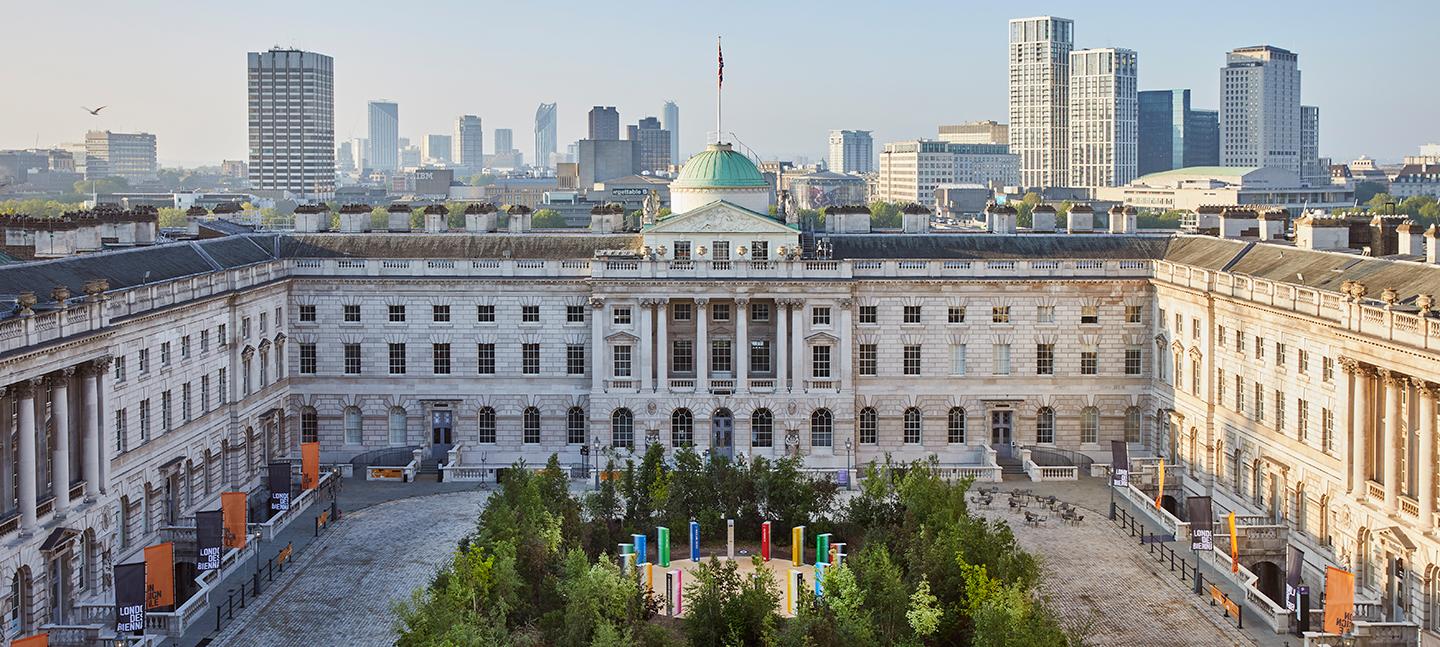 Forest for Change at Somerset House. Green leafy trees fill the courtyard. In the background you can see the London skyline and blue skies.