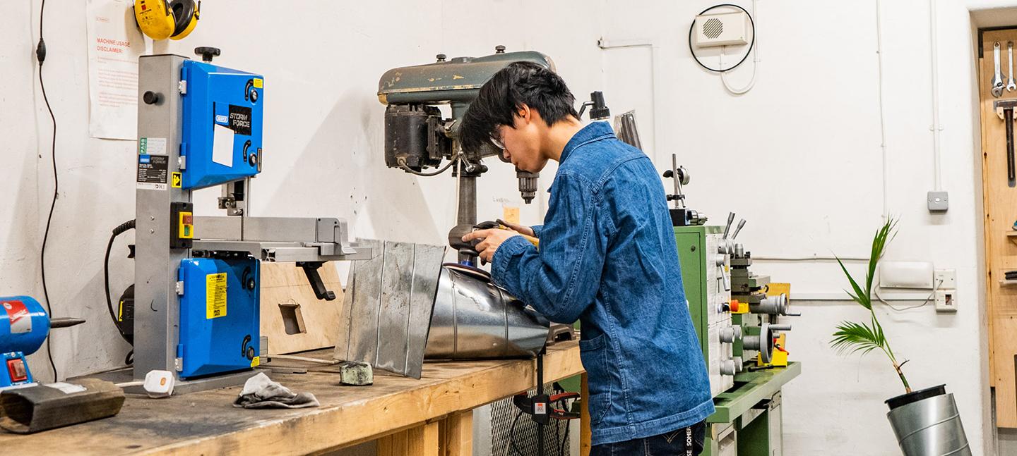 A Makerversity resident works on a metal structure, buffing it with a power tool