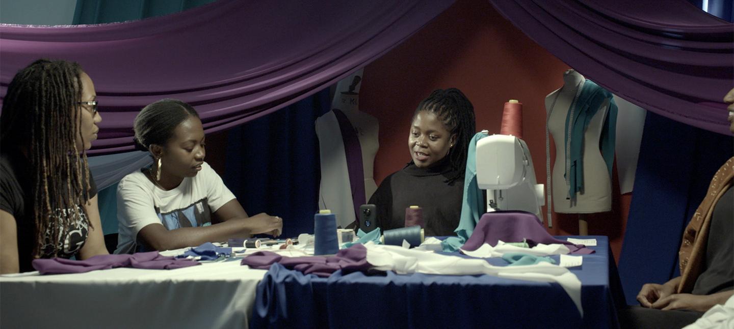 Artist Mary Sibande sitting in a textile studio talking to three women about her work