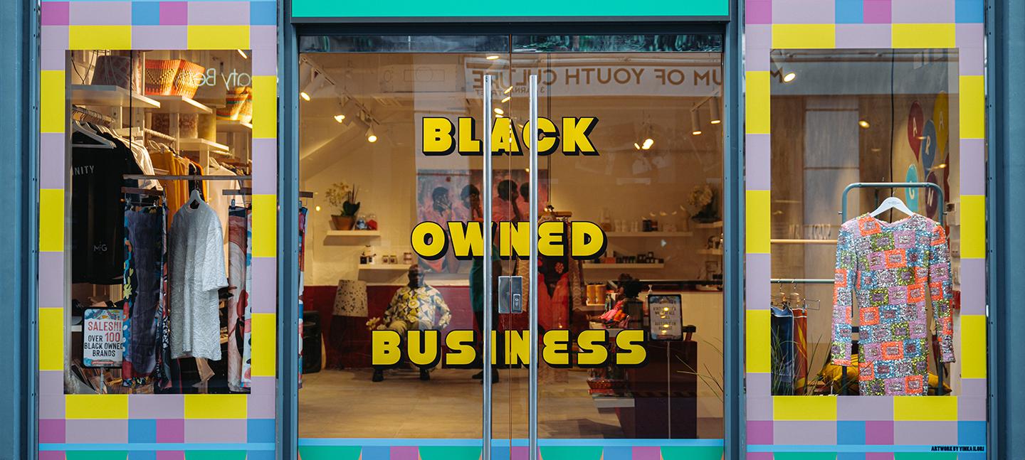 An exterior of a shop. The windows are decorated with bright repeating patterns and on the doors are the words BLACK OWNED BUSINESS