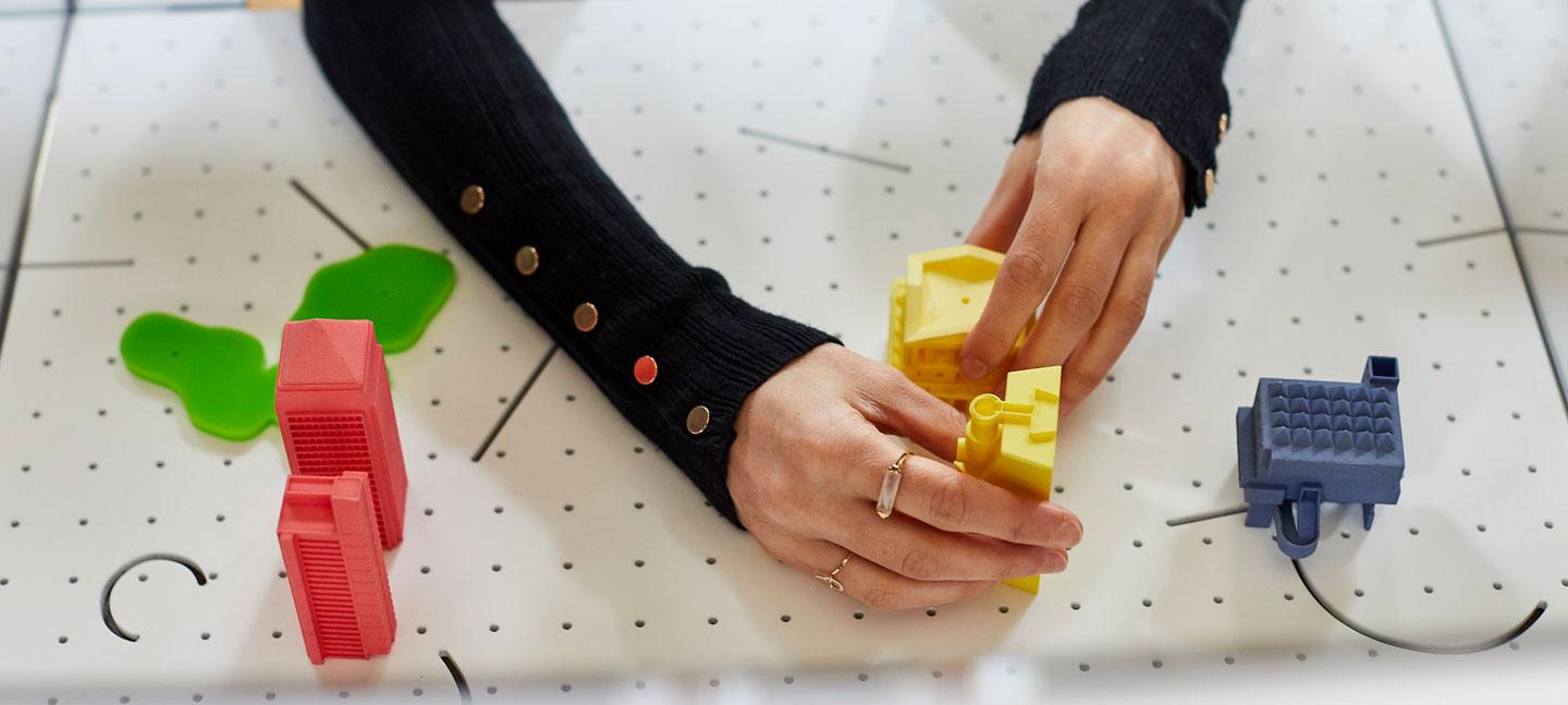 A visitor to the Now Play This projects her hands through a screen to adjust two yellow blocks on a board cut with pin holes. Photo by Ben Peter Catchpole