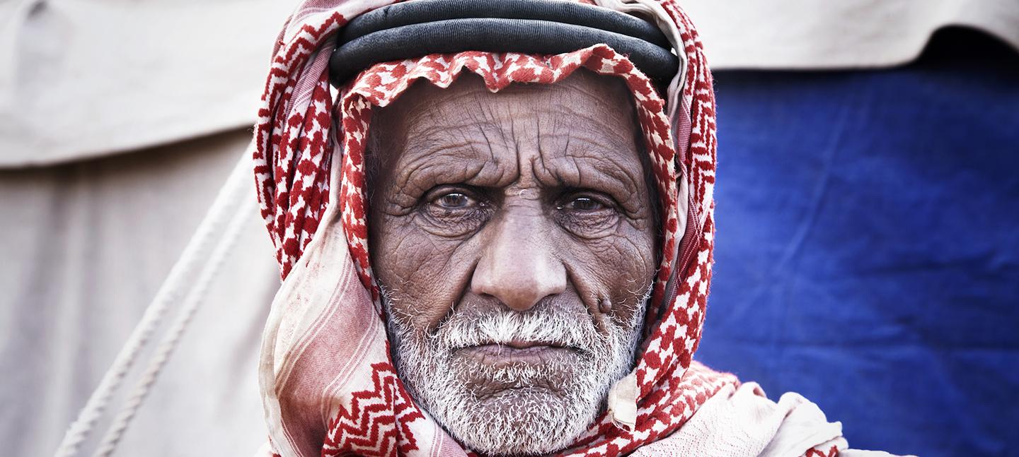 A photo of an old man wearing a head dress, looking straight into the camera, frowning slightly.