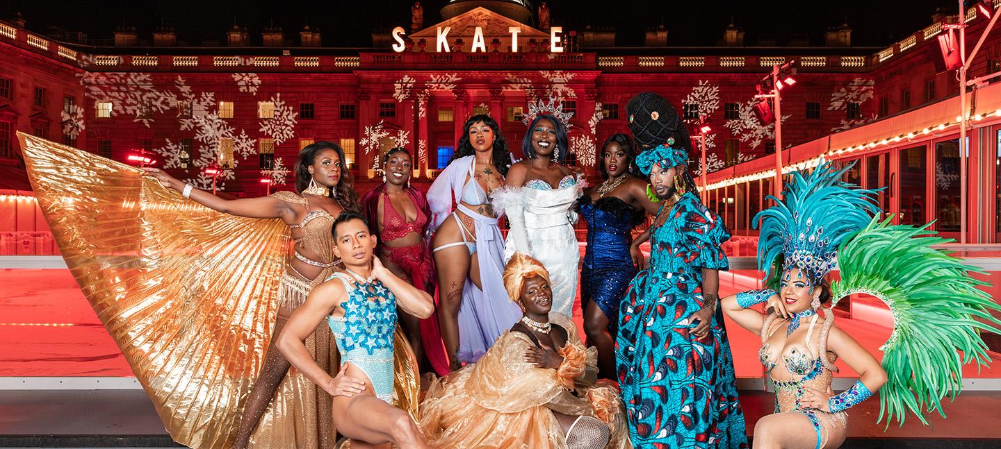 The Cocoa Butter Club pose in front of the ice rink at Somerset House. They are a group of cabaret performers, each wearing ornate, stunning gowns, feathers and sequins in bold bright colours.