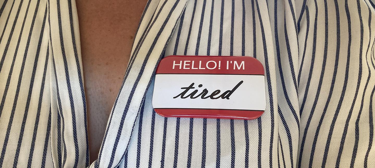 A photo of a person's upper chest, with a sticker on it that reads 'Hello! I'm tired'