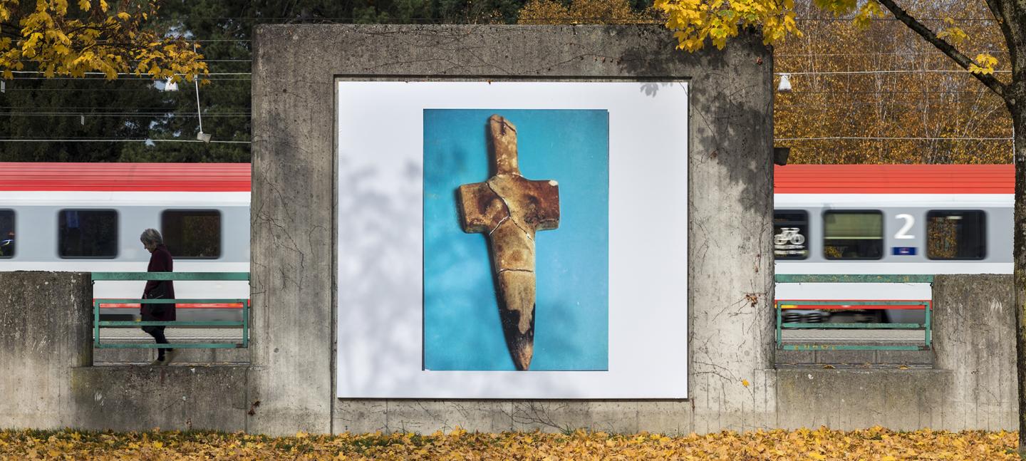 An artwork by Maeve Brennan showing a poster of a stone dagger on a blue backdrop, pasted on a concrete wall by railway tracks