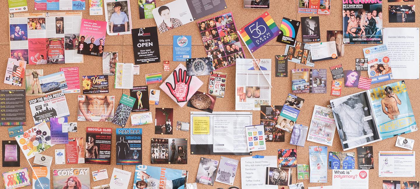 Installation view of UK Gay Bar Directory. The image shows an artwork presenting flyers and flags from different gay bars.