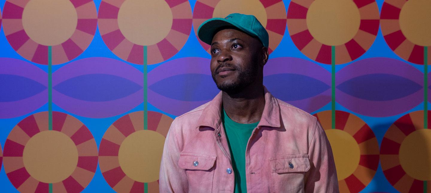 A portrait of designer Yinka Ilori at Somerset House, against a backdrop showing one of his bold, colourful patterns, photo by Stephen Chung