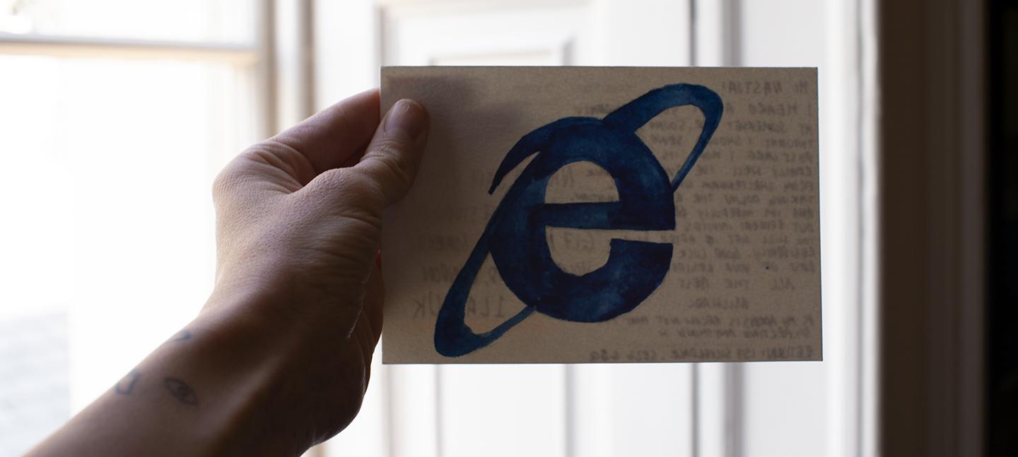 A photo of a hand holding a postcard. On the front of the postcard is the letter e in blue.