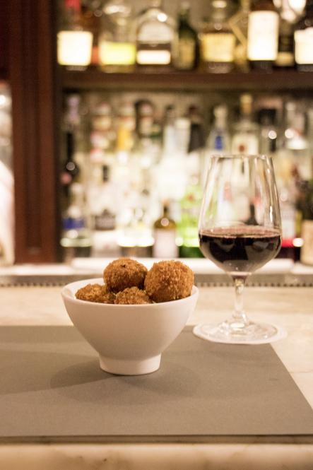 A bowl of mushroom arancini and a glass of red wine on the bar at Cafe Murano