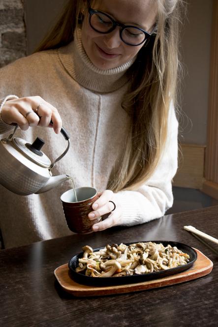 A woman pours a cup of green tea in from of a plate of stir-fried mushrooms at Eat Tokyo