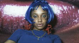 A photo by Eileen Perrier shows a confident young woman with blue bobbed hair lookign directly at the viewer 