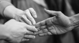 A black and white photo of three different hands, the tips of their fingers touching at the center of the image