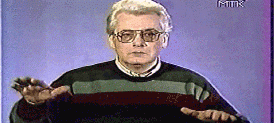 A GIF of Alan Chamuk. The image depicts an old man in grey hair and glasses looking at the camera. The background is blue.